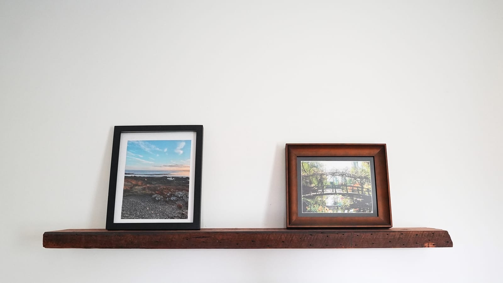 Long wood floating shelf on a white wall with two framed pictures on it